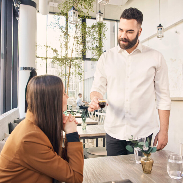 A waiter serves a seated woman a coffee in a café.