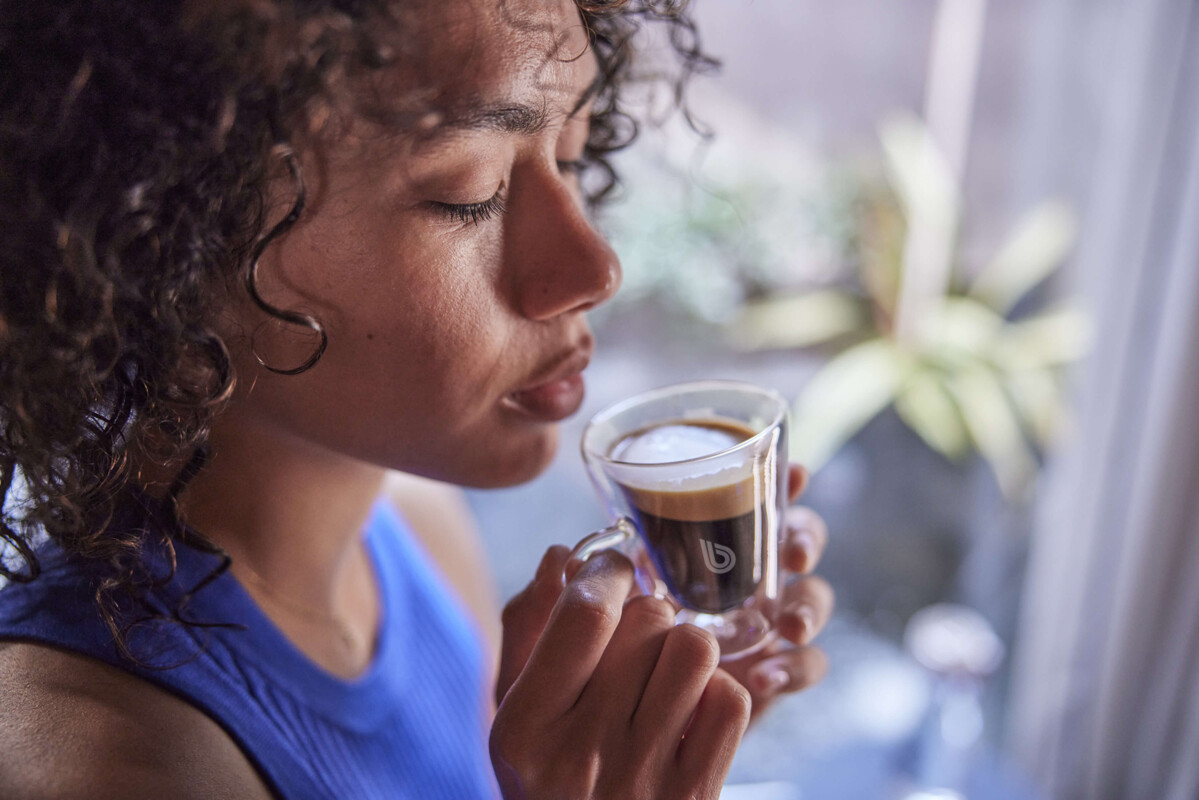 Eine Frau hält eine gläserne Espressotasse mit BWT-Logo und genießt den aromatischen Duft frischen Kaffees.